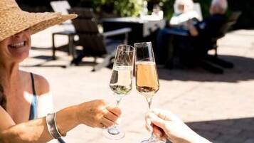 Zwei Personen stoßen mit Champagnergläsern bei einem Tisch im Freien an, mit einer Schüssel Essen und einem Brotbrett.