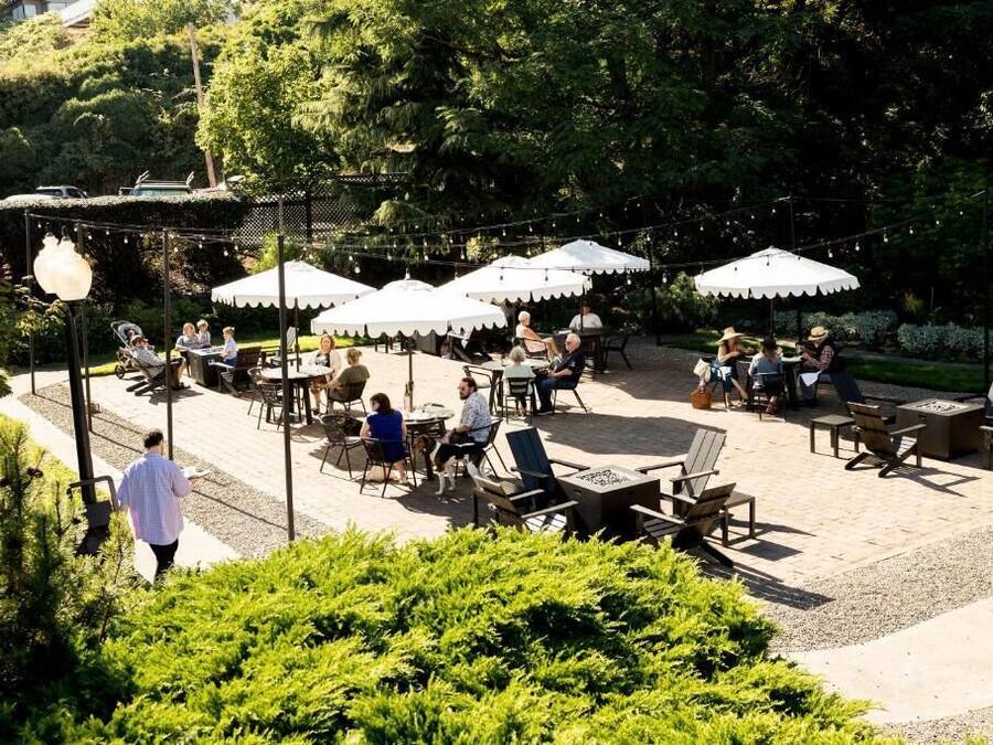 En udendørs terrasse med borde og stole, omgivet af grøn vegetation og parasoller.