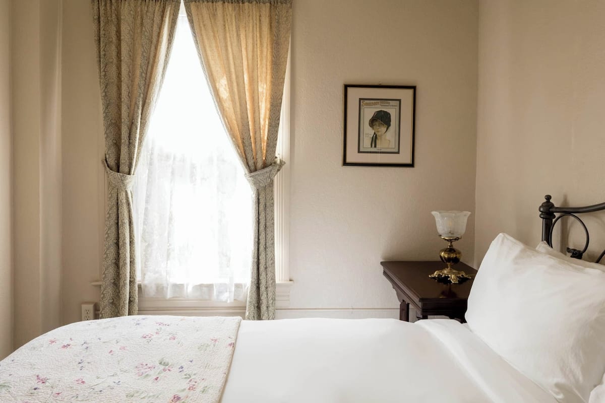 A hotel room with a bed, a nightstand, a lamp, and a framed picture on the wall.