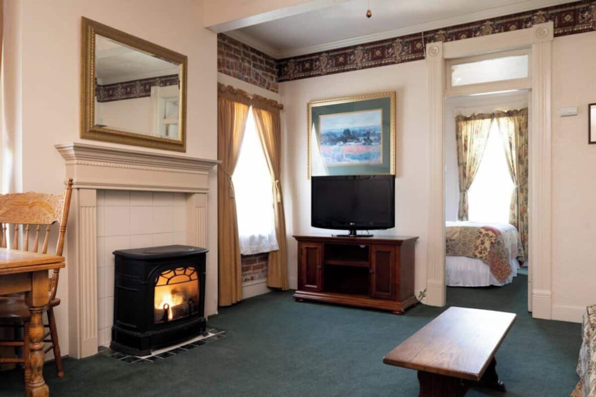 A cozy room with a fireplace, a television, a wooden table, and a bed with floral curtains.