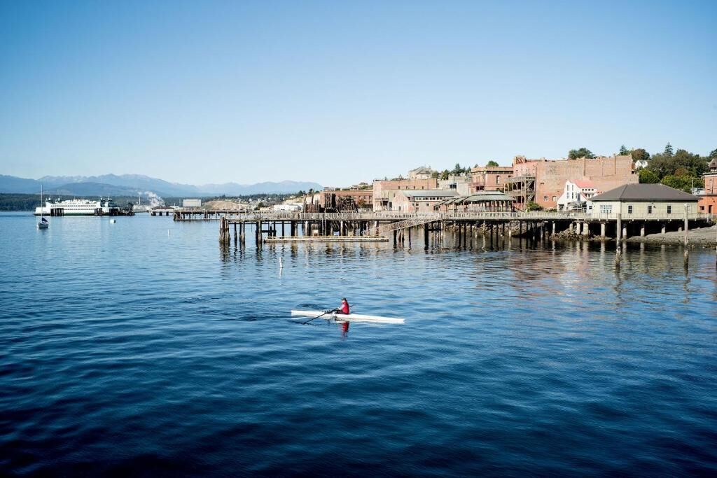 A calm waterfront with a rowboat, a pier, and buildings in the background.