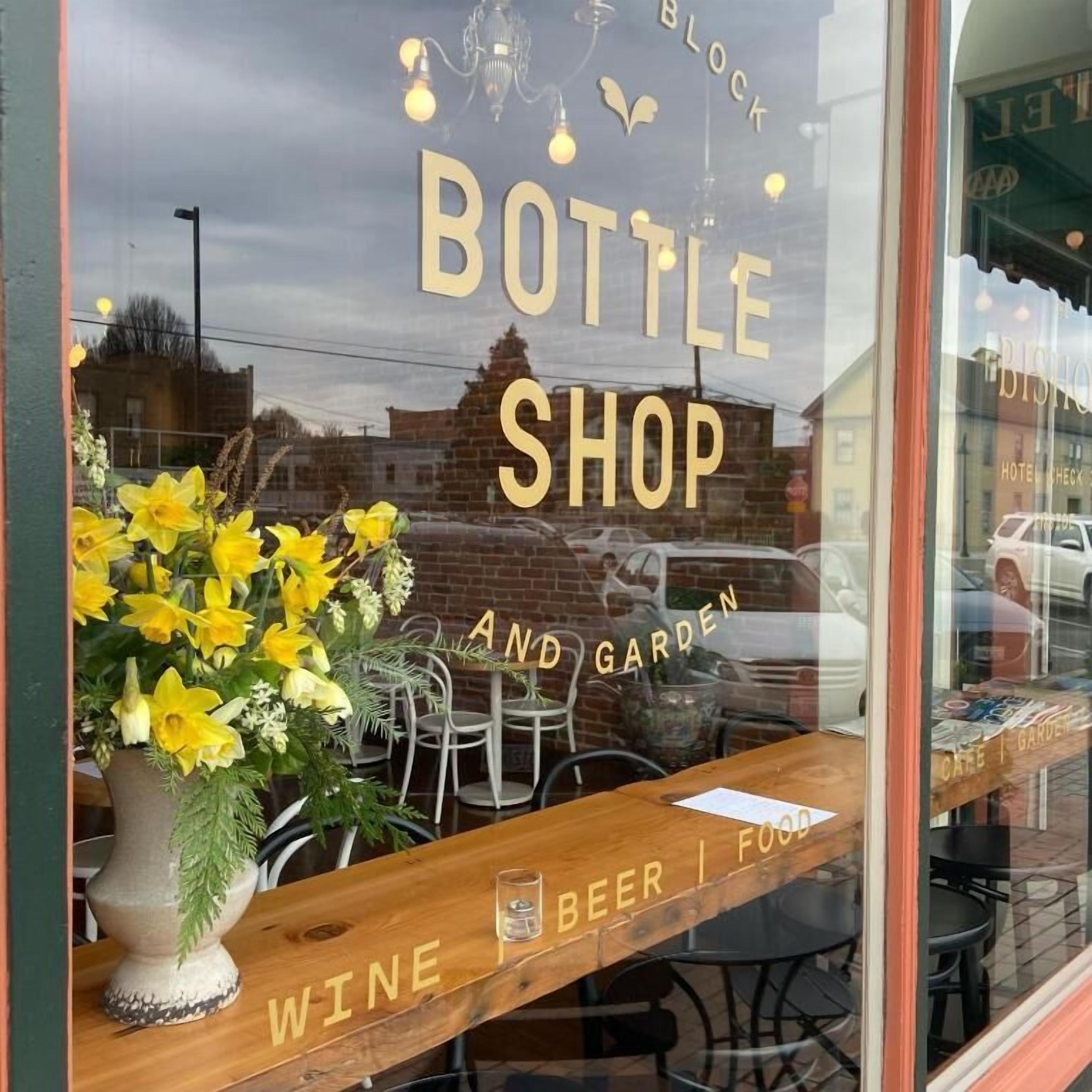 A window display for a Bottle Shop with a wooden signboard and a vase of yellow flowers.