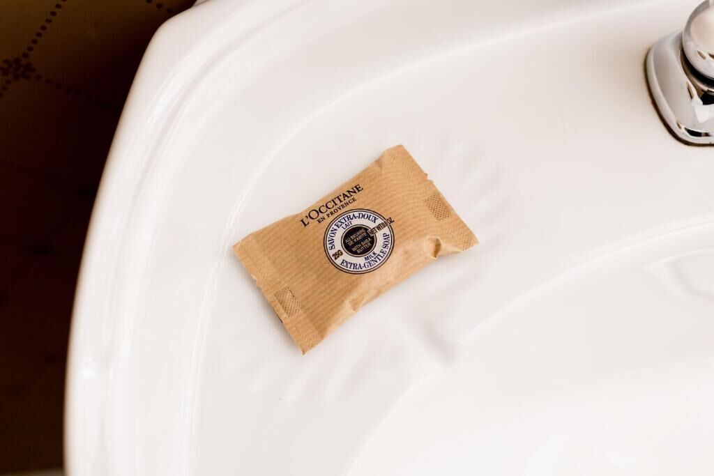 A white toilet with a brown paper bag labeled "L'OCCITANE" on it.