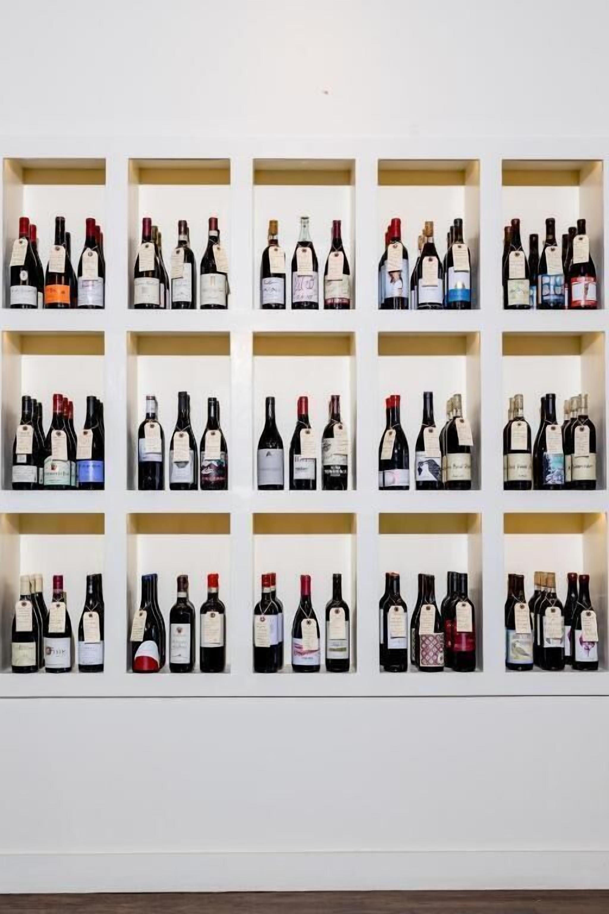 A wall with multiple rows of wine bottles displayed in white shelves.