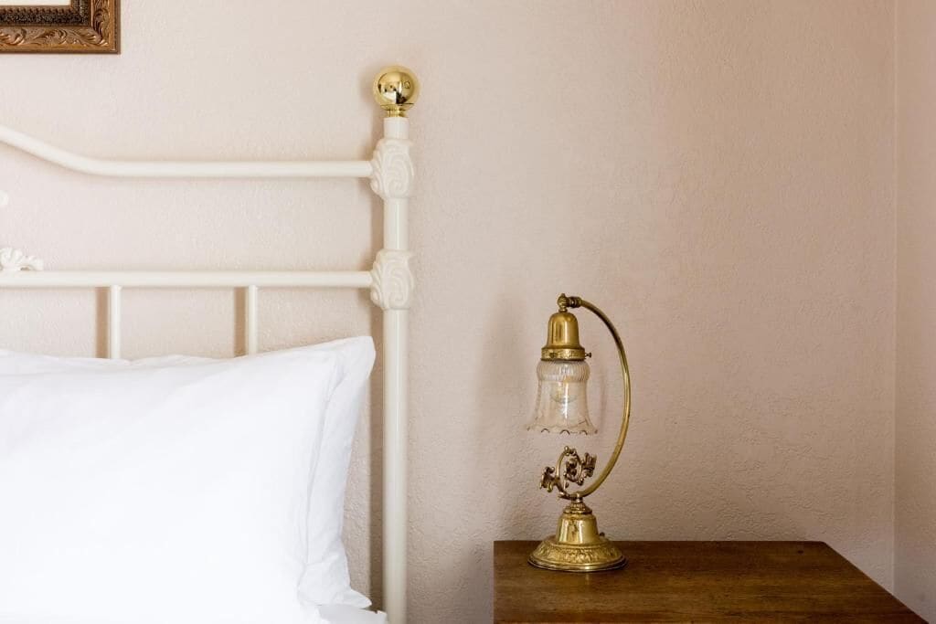 A bed with a white headboard and a bedside table with a brass lamp.