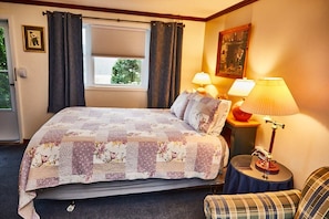Relax in a serene space with a large bed, floral-patterned quilt, and a view of lush greenery.