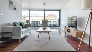 Una sala de estar moderna con un sofá, una mesa de centro, televisor y un ventanal con vistas a la ciudad.