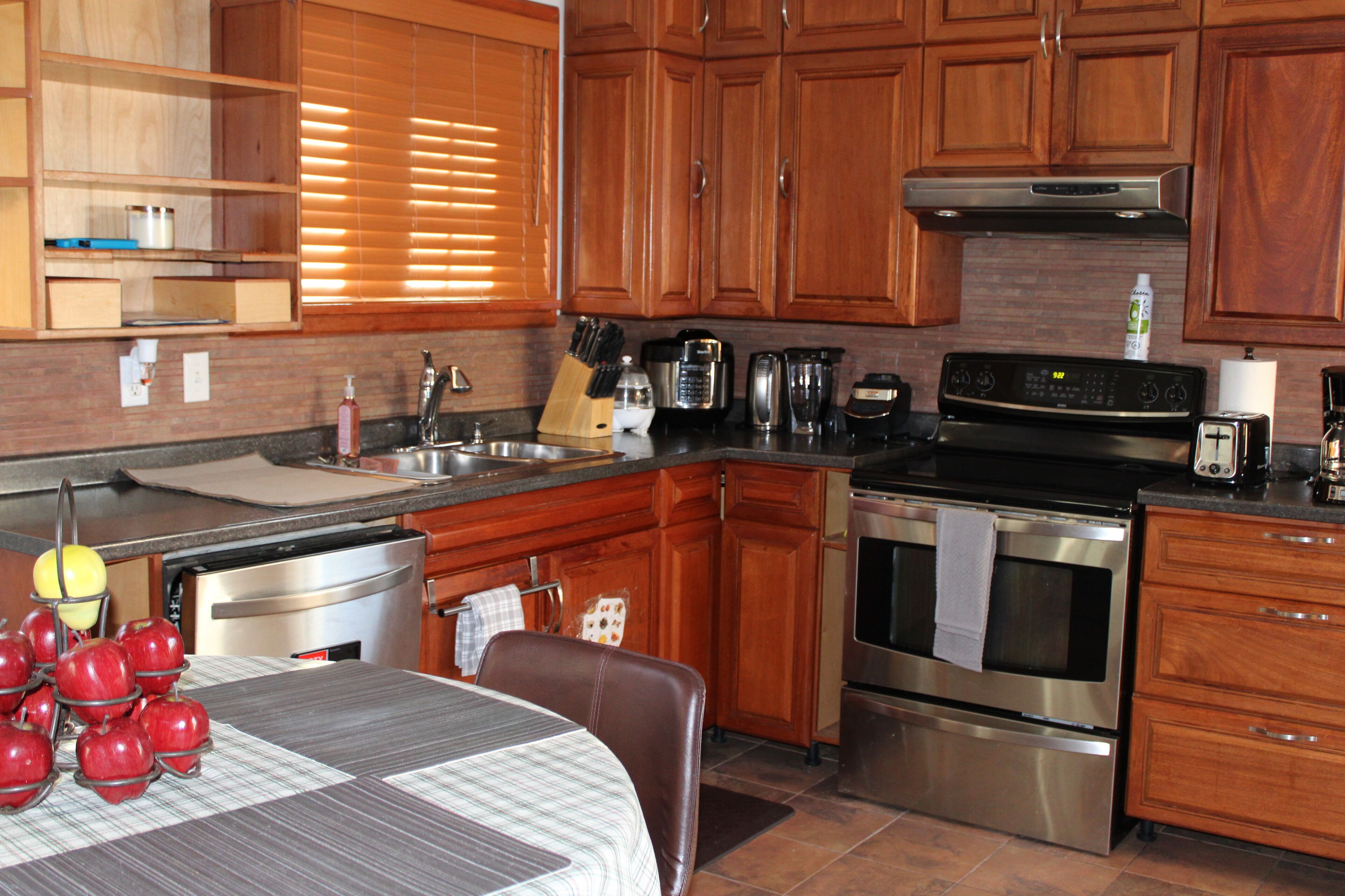 Una cocina con armarios de madera, electrodomésticos de acero inoxidable y una zona de comedor con una mesa preparada para dos.