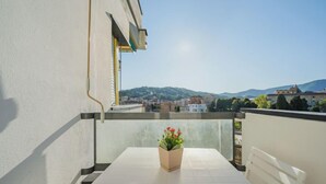 A balcony with a white table and a potted plant, overlooking a cityscape with buildings and hills.