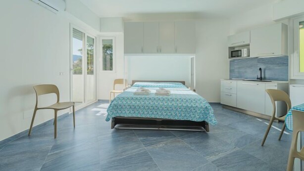 A bedroom with a bed, a chair, a small table, and a kitchenette.