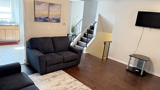A living room with a dark grey sofa, a patterned rug, a flat-screen TV, and a staircase leading to another level.