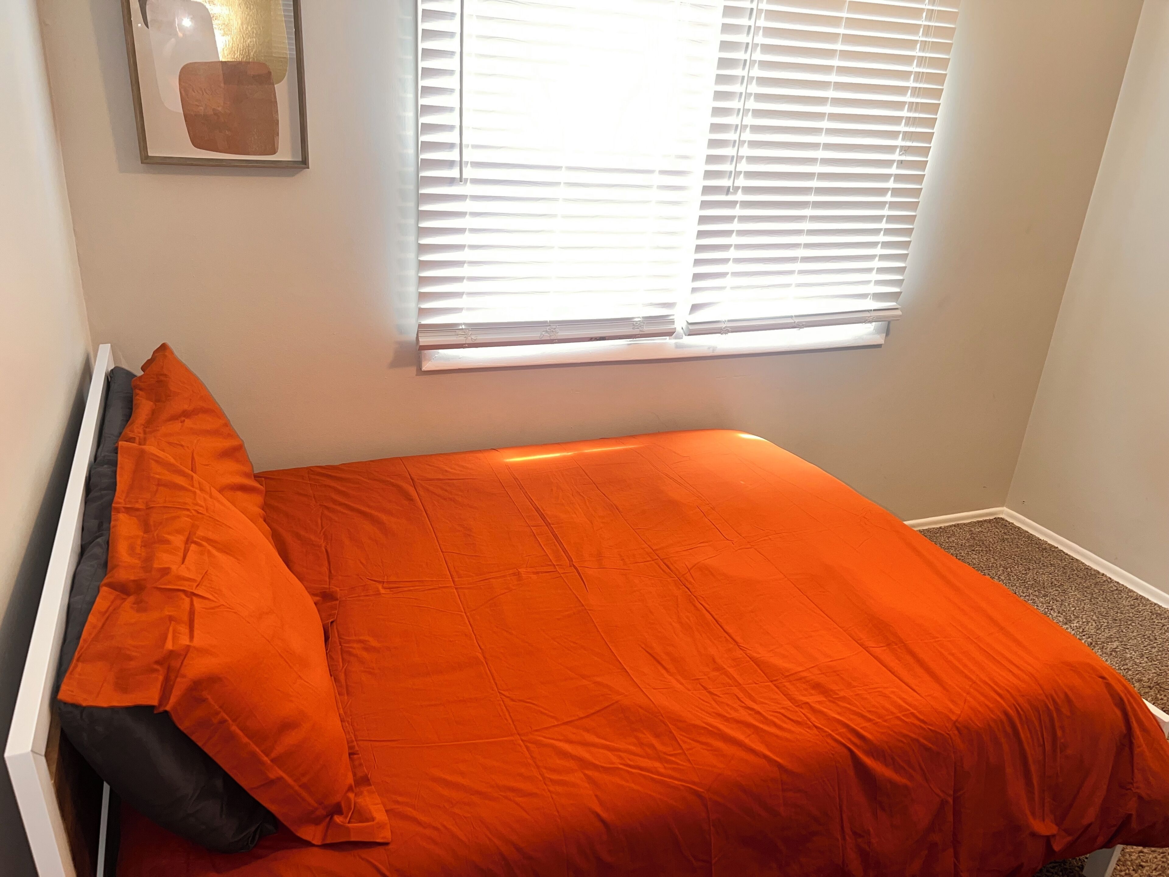 Un petit lit bien fait, avec une couverture orange et un oreiller noir.