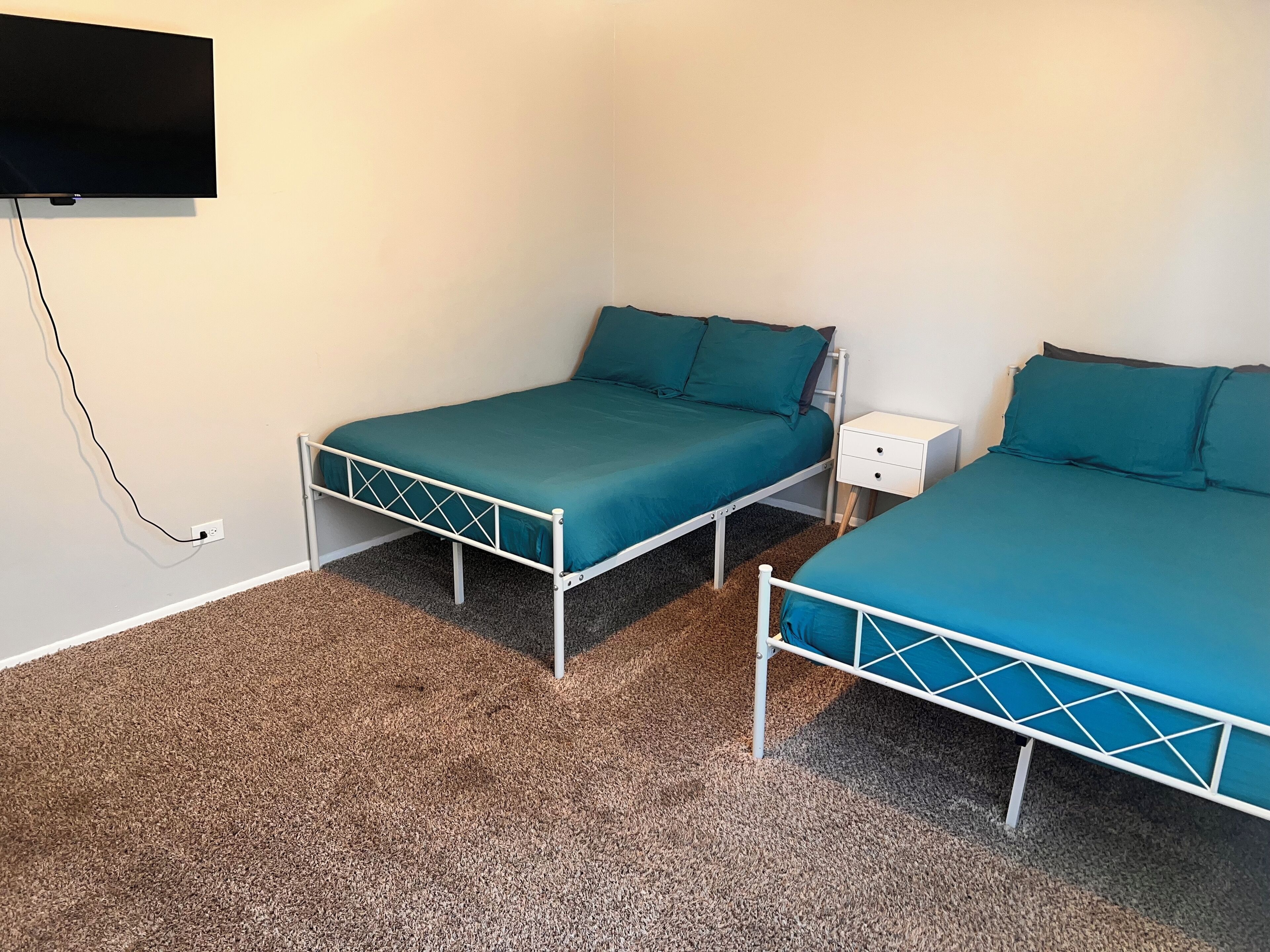 A room with two single beds, a white nightstand, and a TV mounted on the wall.