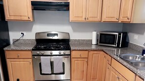 A kitchen with wooden cabinets, a stainless steel stove, a microwave, and a red rug.