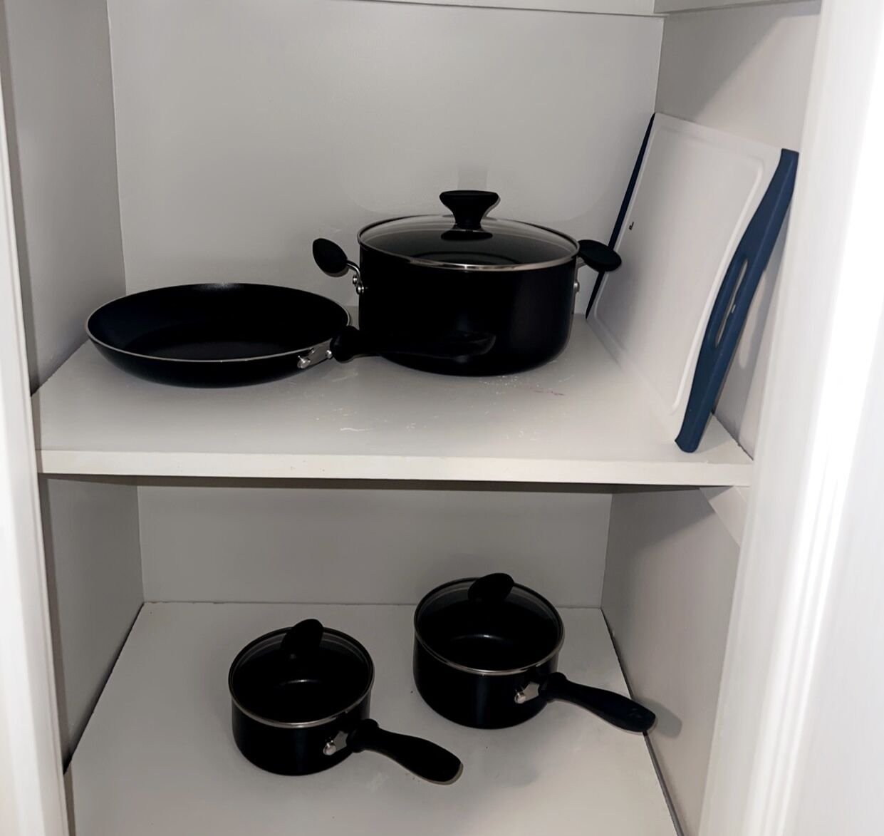 A kitchen with white shelves, a black frying pan, a black pot, and two black pans.