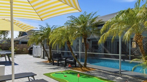 A poolside area with a mini-golf setup, outdoor seating, and a large striped umbrella.