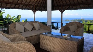 A covered outdoor seating area with wicker furniture and a view of the ocean. - Villa Kipas Retreat (Senggigi)