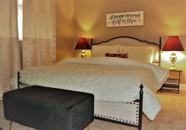 A bedroom with a bed, bedside lamps, a bench, and a wall sign.