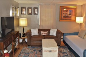 Ein Wohnzimmer mit braunem Sofa, einem Fernseher, einer Lampe und einem gerahmten Bild an der Wand.
