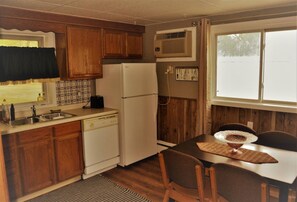 A compact kitchen with wooden cabinets, a white refrigerator, and a dining table with chairs.