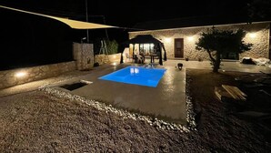 A swimming pool with a blue surface, surrounded by a stone wall and a wooden deck. - Villa with pool in Pelekas near the beach (Pelekas)