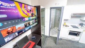 Une chambre d’hôtel équipée d’une grande télévision diffusant un film, d’un ordinateur portable, d’un téléphone intelligent, d’une douche et d’une kitchenette.