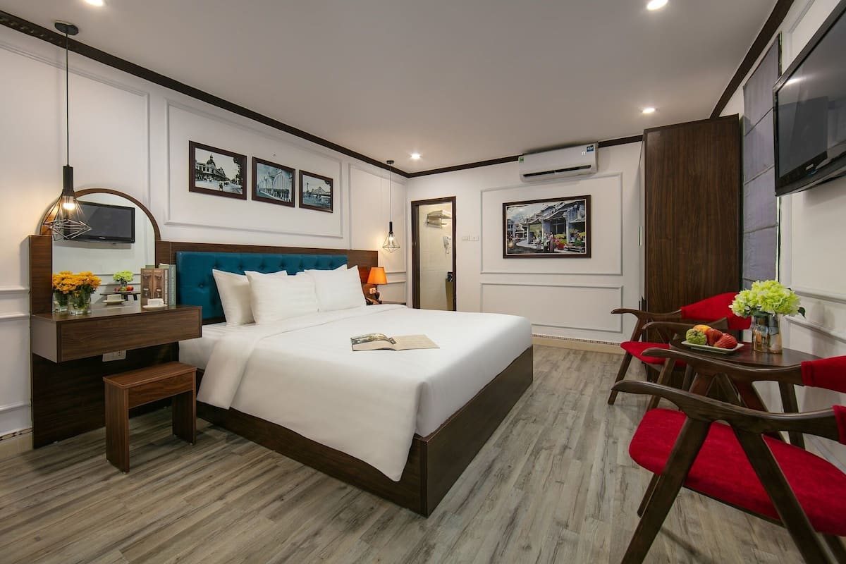 Een hotelkamer met een groot bed, een bureau met stoel, een televisie en kunstwerken aan de wanden.