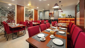Un restaurant avec des chaises rouges, des tables en bois et des luminaires suspendus.