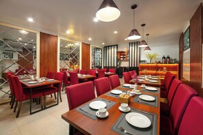 A restaurant with red chairs, wooden tables, and pendant lighting. - Silk Hanoi Moment Hotel & Spa (Hanoi)