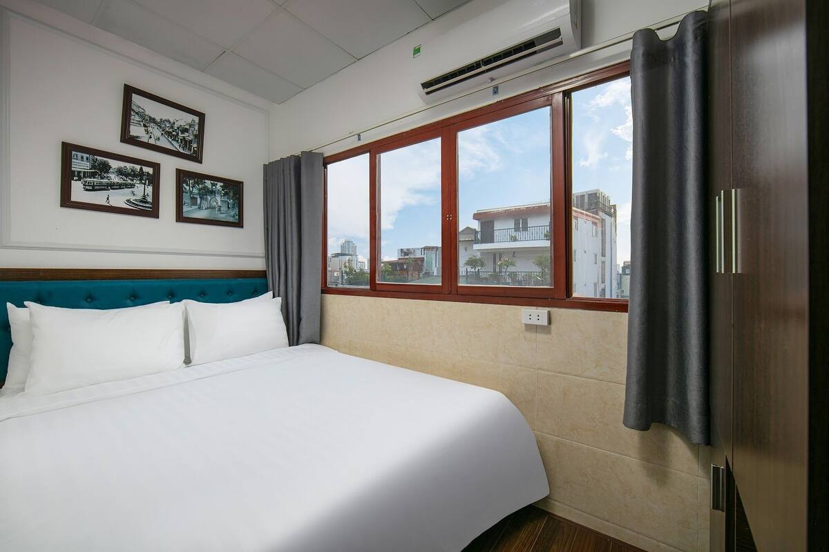 Een hotelkamer met een bed, uitzicht op gebouwen en een raam met gordijnen.