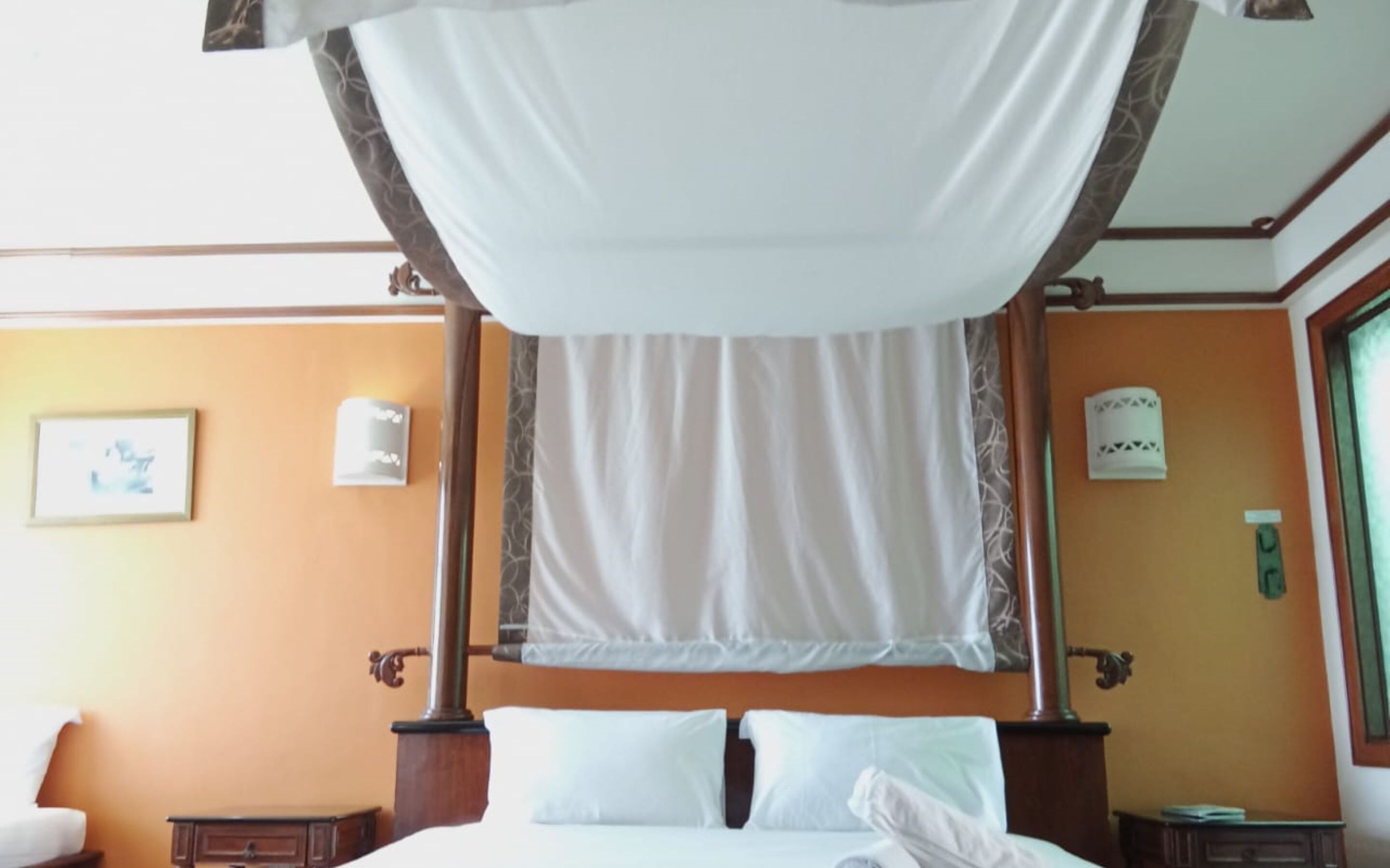 Quarto com cama de dossel, mesa de cabeceira e luminária fixa na parede.