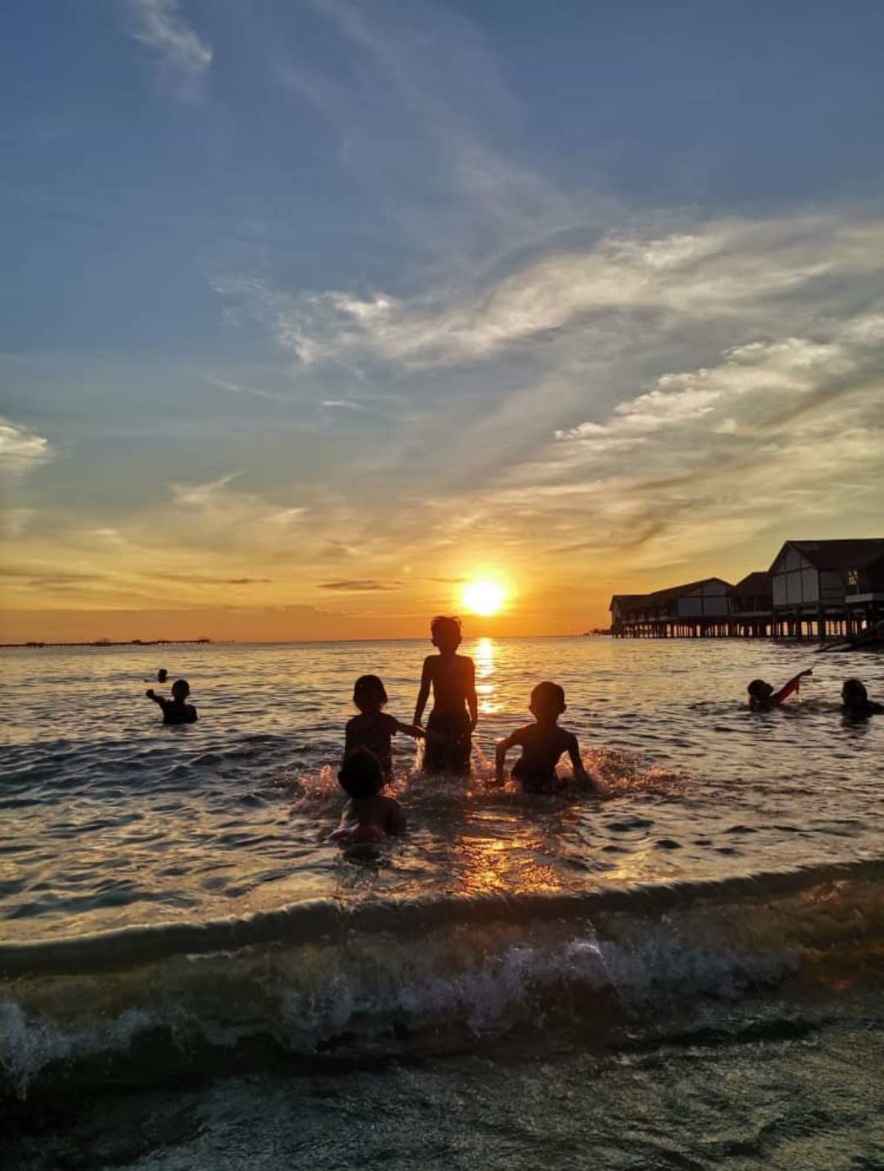 A sunset over a body of water with people in the water and a building in the background.