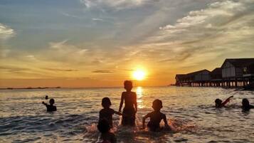 A sunset over a body of water with people in the water and a building in the background.