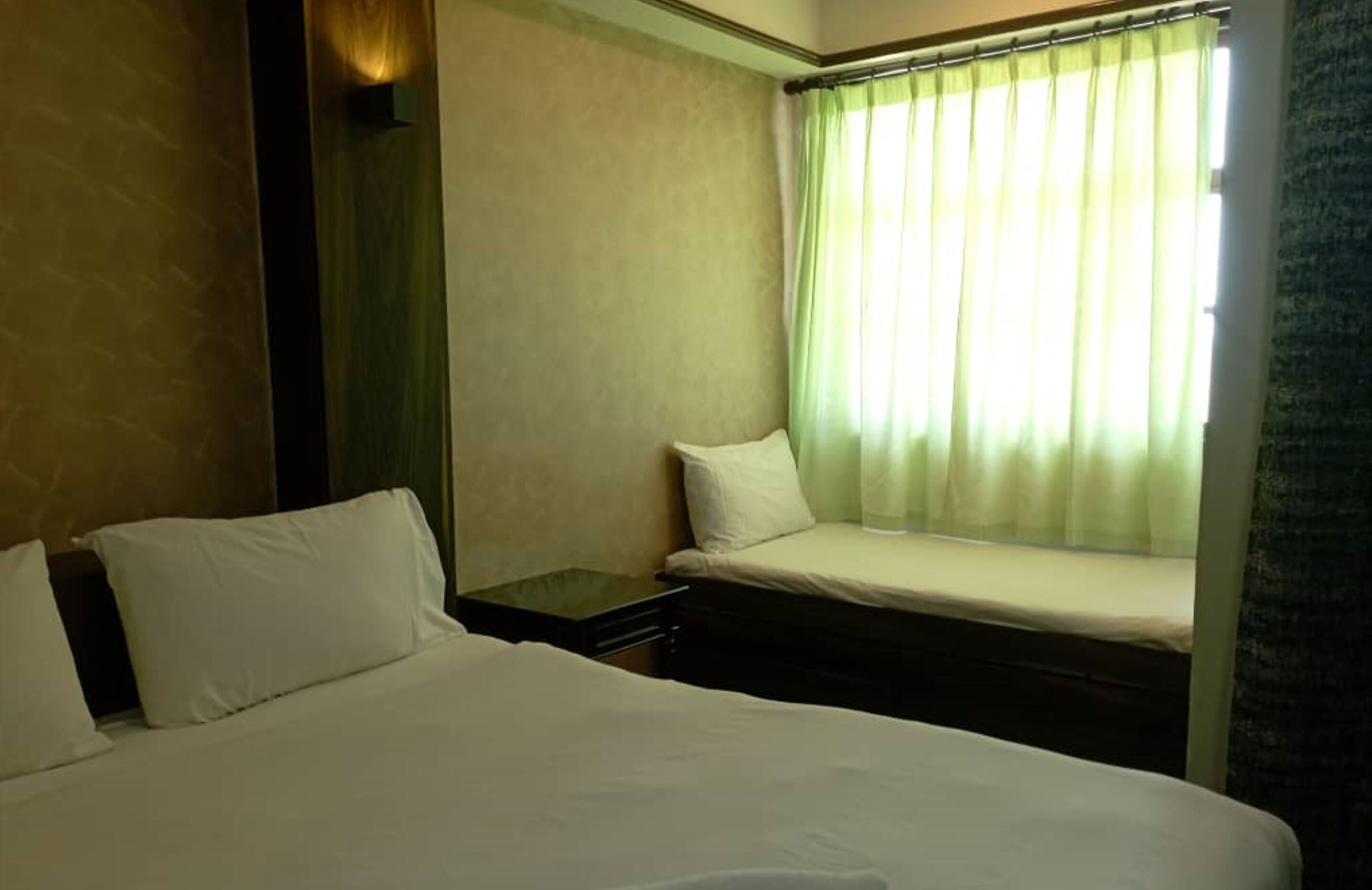 A hotel room with a bed, a small bench, and a window with curtains.