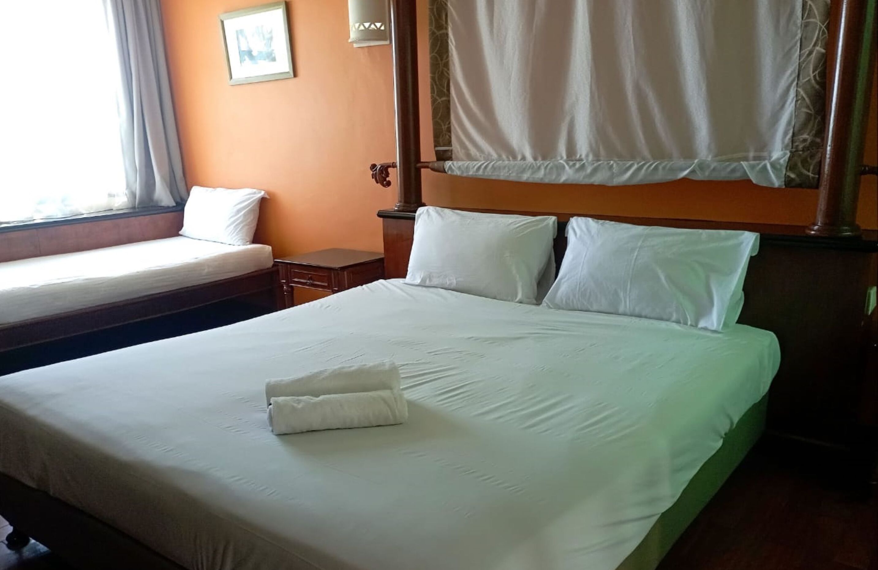 A hotel room with two beds, a mosquito net, and a small bedside table.