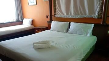 A hotel room with two beds, a mosquito net, and a small bedside table.