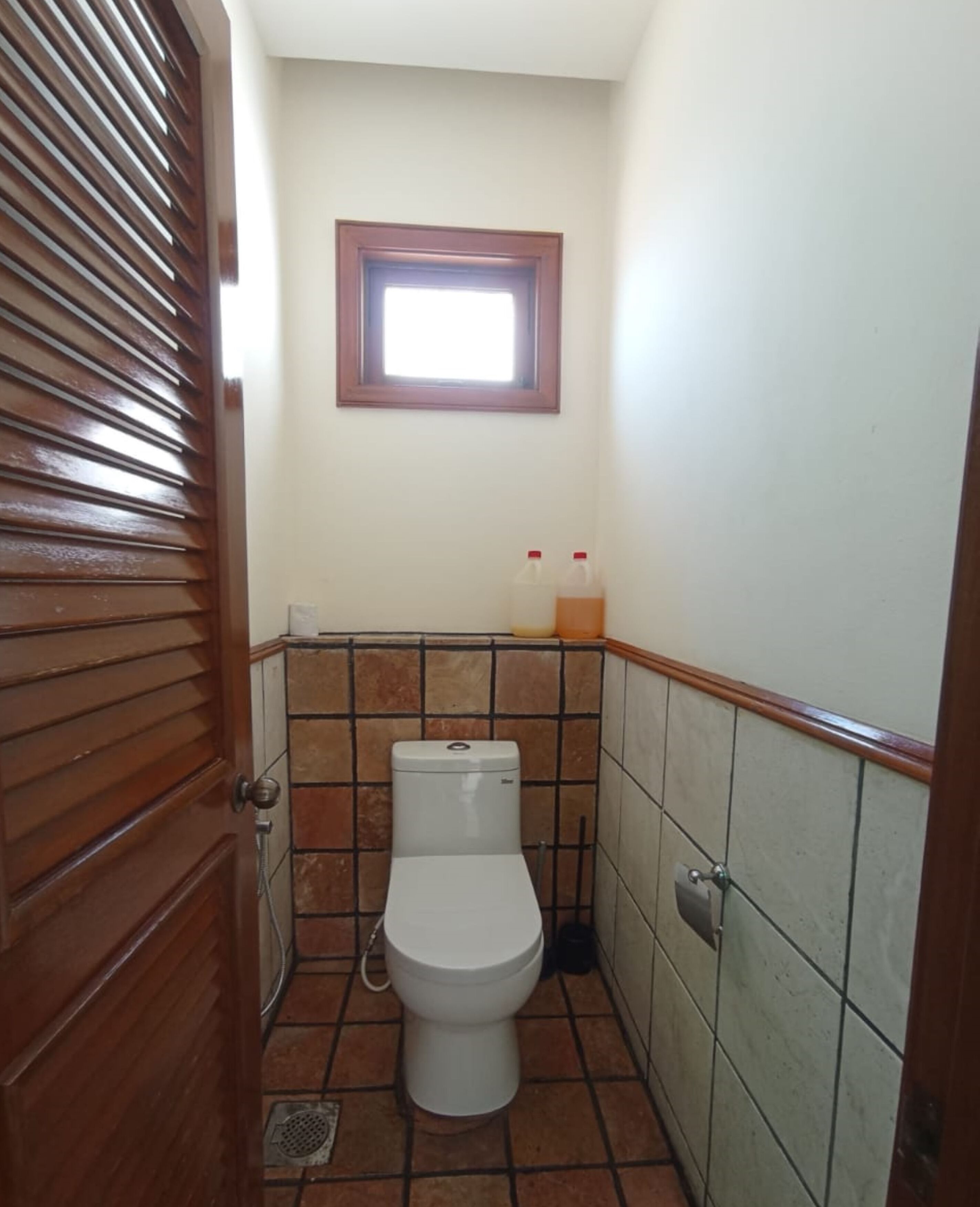 Un baño pequeño con inodoro, ventana y pared con azulejos.