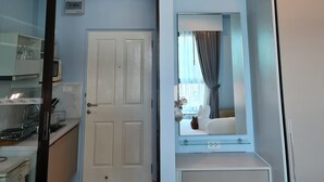 Habitación de hotel con kitchenette, una puerta blanca, un espejo sobre un tocador y un ventilador de techo.
