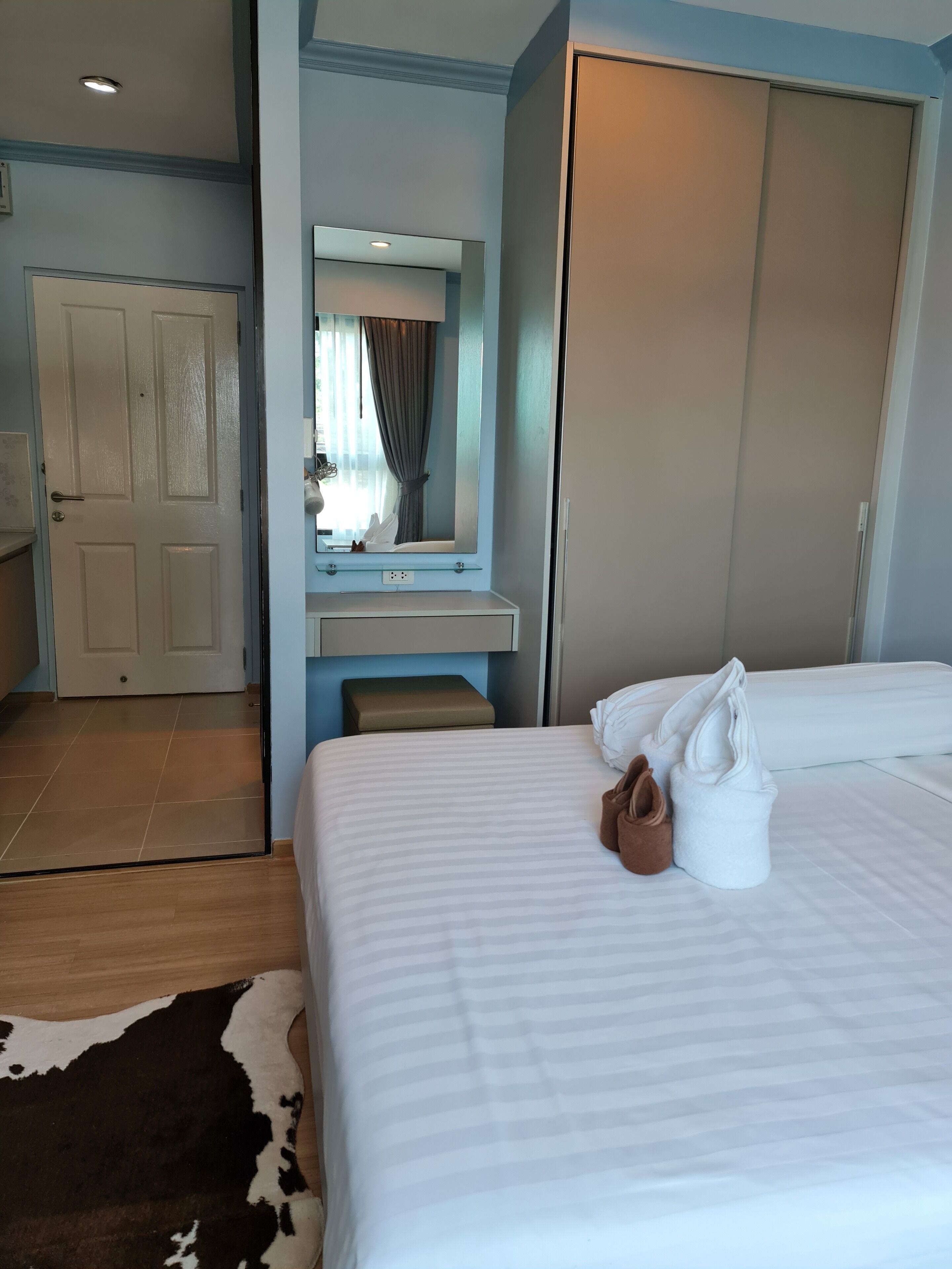 A hotel room with a bed, a mirror, a wardrobe, and a small bench.