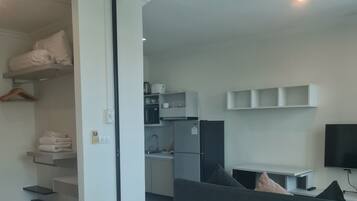 A modern hotel room with a bed, a desk, a kitchenette, and a TV.