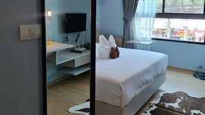 Habitación de hotel moderna con una cama grande, un televisor de pantalla plana, un escritorio con lámpara y vistas al exterior por una ventana.