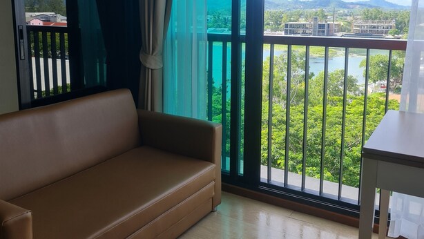 Una habitación con un sofá marrón, una mesita y un ventanal con vistas a un paisaje verde y edificios.