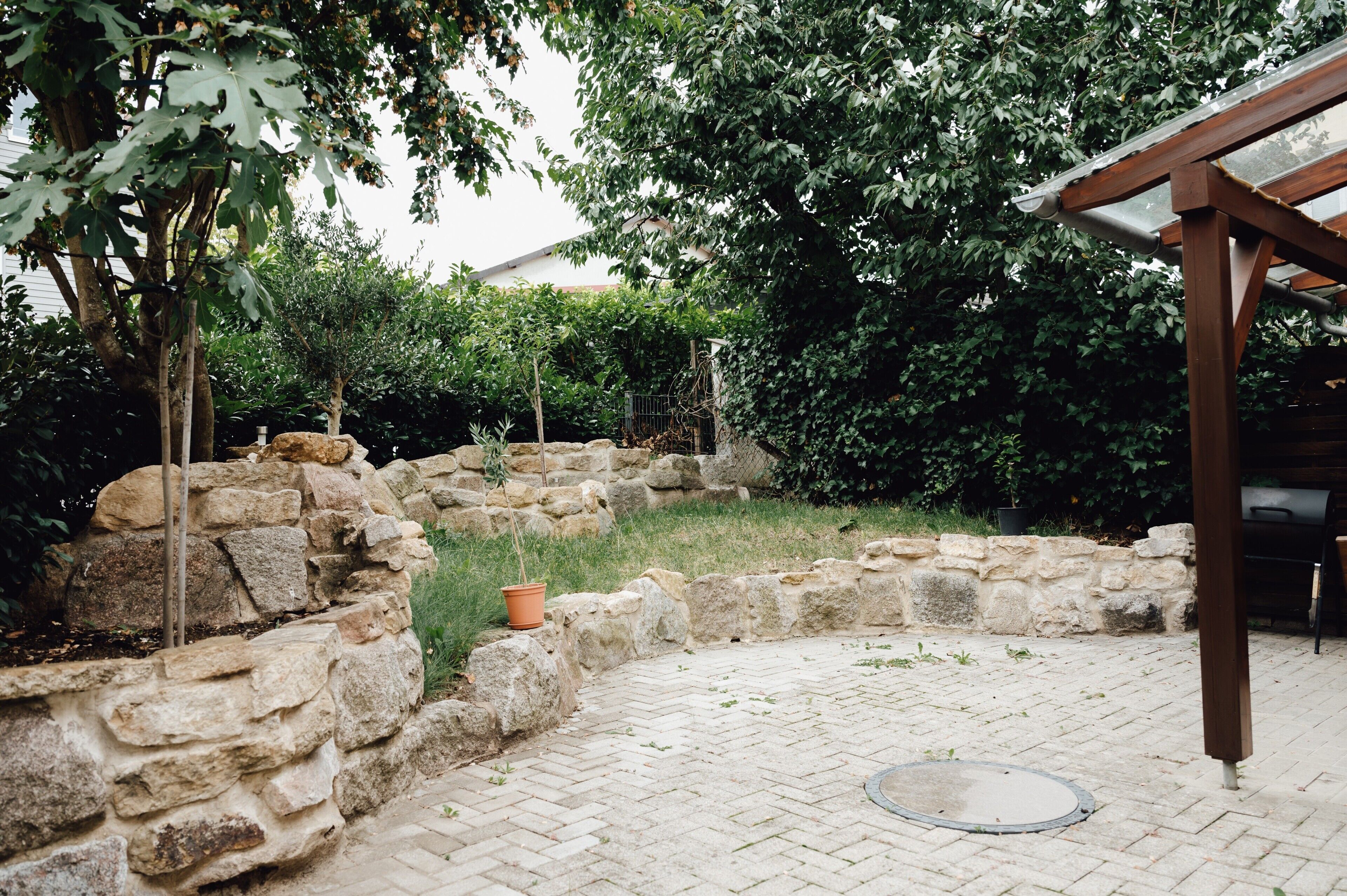 Un mur en pierre, une pergola en bois et une terrasse dallée.