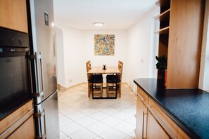 A kitchen with a dining table, chairs, a refrigerator, and a wall-mounted artwork.