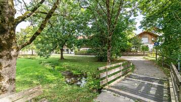 Ein Parkweg mit einer Holzbank, einem kleinen Bach und einem Gebäude im Hintergrund.