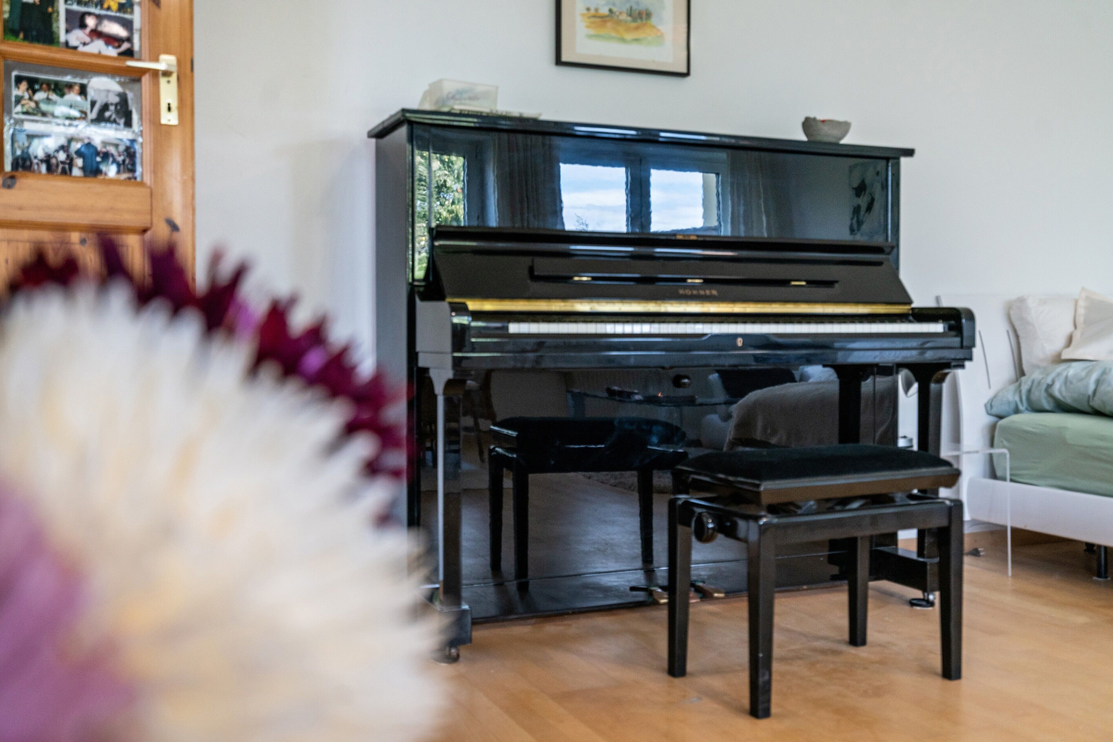 Ein Klavier in einem Raum mit Holzboden, einem weißen Stuhl und einem gerahmten Bild an der Wand.