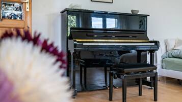 Ein Klavier in einem Raum mit Holzboden, einem weißen Stuhl und einem gerahmten Bild an der Wand.