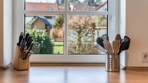 Keittiön ikkuna, josta avautuu näkymä asuinalueelle, puinen veitsiteline ja metallinen aterinteline.