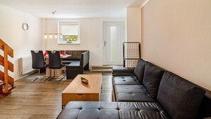 A modern living room with a sectional sofa, a wooden coffee table, and a dining area with chairs and a table. - Holiday Apartment "Nordsee 1" with Shared Terrace, Shared Garden & Wi-Fi (Wangerland)