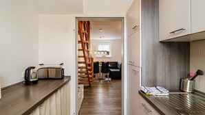 A modern kitchen with wooden flooring, a built-in stove, and a dining area with a chair and table. - Holiday Apartment "Nordsee 1" with Shared Terrace, Shared Garden & Wi-Fi (Wangerland)